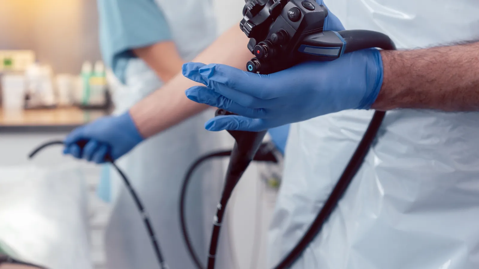 Two gowned staff handling a flexible endoscope during reprocessing